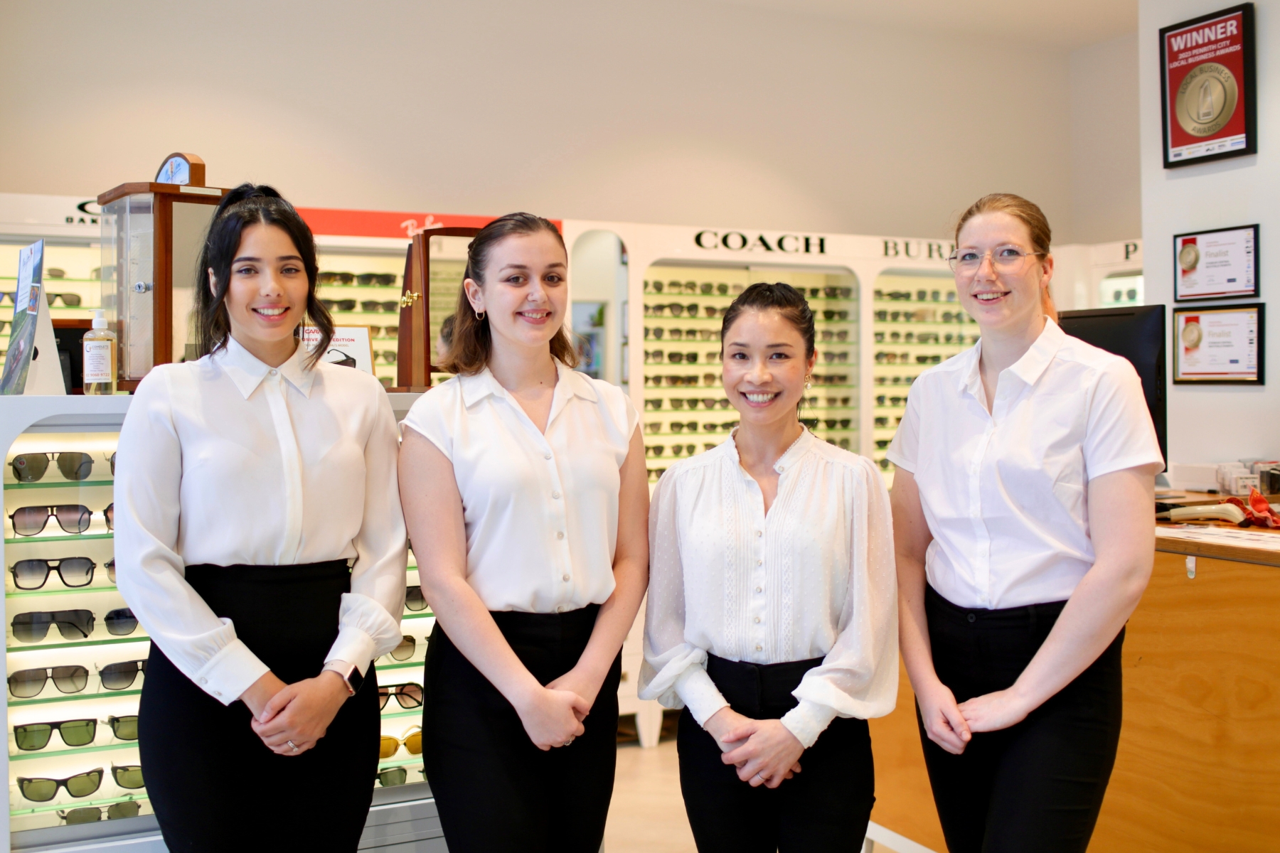 Team photos of 4 females all wearing white shirt and black pants in an optical shop